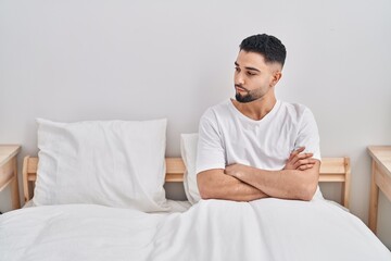 Young arab man sitting on bed with angry expression and arms crossed gesture at bedroom