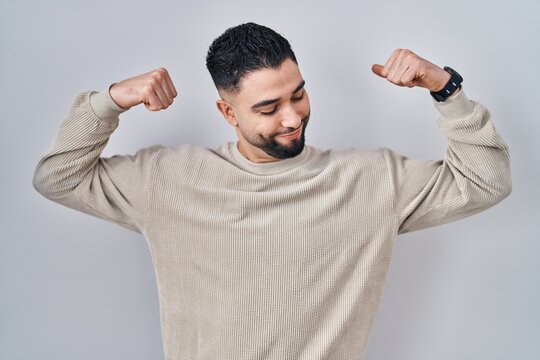 Young handsome man standing over isolated background showing arms muscles smiling proud. fitness concept.