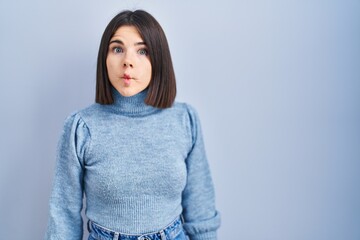 Young hispanic woman standing over blue background making fish face with lips, crazy and comical gesture. funny expression.