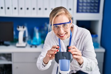 Young blonde woman scientist smiling confident using microscope at laboratory