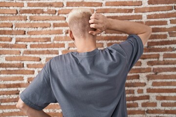 Young caucasian man standing over bricks wall backwards thinking about doubt with hand on head