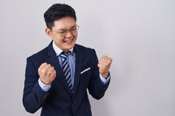 Young asian man wearing business suit and tie very happy and excited doing winner gesture with arms raised, smiling and screaming for success. celebration concept.
