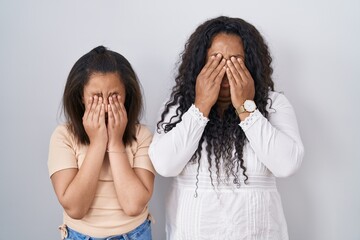 Mother and young daughter standing over white background rubbing eyes for fatigue and headache,...