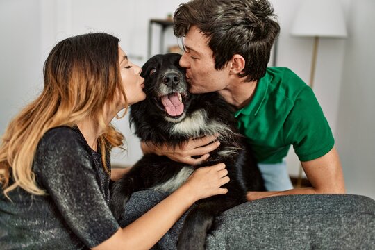 Young caucasian couple smiling happy hugging and kissing dog at home.