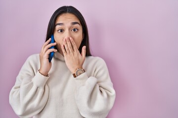 Young south asian woman having conversation talking on the smartphone covering mouth with hand,...