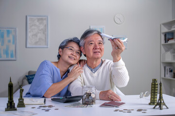 Happy Asian senior couple plans to save money for a trip around the world .Travel budget concept, passport monument model and aircraft toy in the picture.