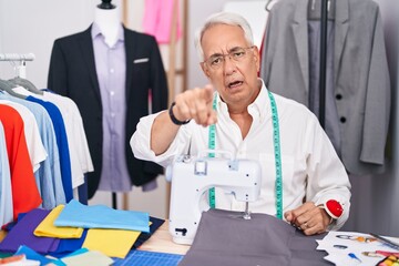 Middle age man with grey hair dressmaker using sewing machine pointing displeased and frustrated to the camera, angry and furious with you