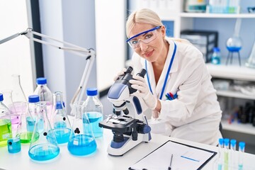 Young blonde woman wearing scientist uniform using microscope at laboratory