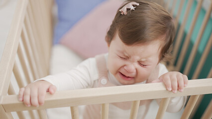 Adorable toddler standing on cradle crying at bedroom