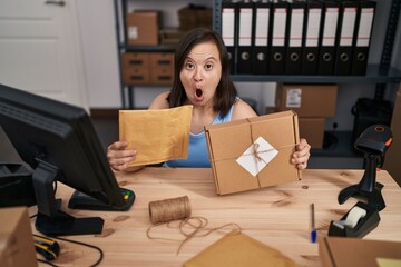 Hispanic girl with down syndrome working at small business ecommerce in shock face, looking...