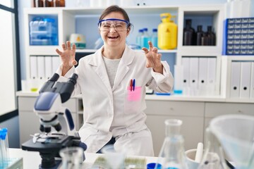 Fototapeta premium Hispanic girl with down syndrome working at scientist laboratory smiling funny doing claw gesture as cat, aggressive and sexy expression