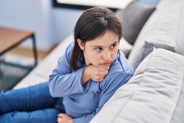 Obraz premium Young woman with down syndrome sitting on sofa with serious expression at home