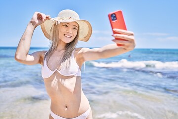 Young chinese girl wearing bikini make selfie by the smartphone at the beach.