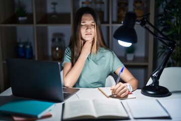 Teenager girl doing homework at home late at night touching painful neck, sore throat for flu, clod...