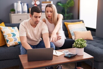 Man and woman couple expecting baby using laptop accounting at home