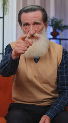 Hey you. Senior bearded man smiling excitedly and pointing to camera, choosing lucky winner, indicating to awesome you, inviting, approve. Elderly mature grandfather at home room. Vertical view shot