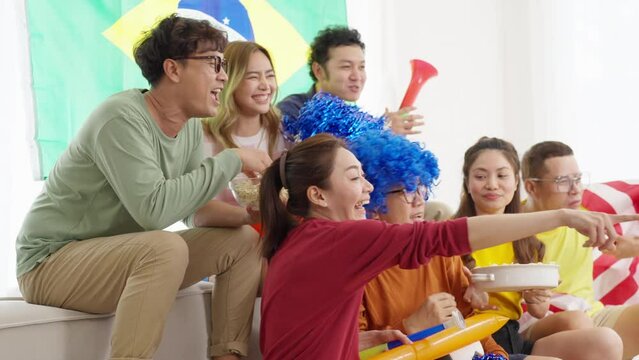 4K Asian man and woman sport fans shouting and celebrating football team victory the match during watching world soccer football competition on television with eating food and drinking beer at home.