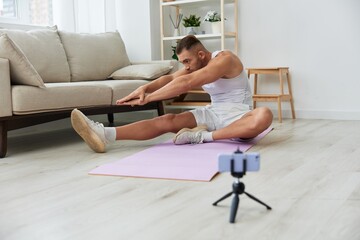 Man sports, watching a workout tape on his phone and repeating exercises blogger, pumped up man fitness trainer works out at home, the concept of health and body beauty