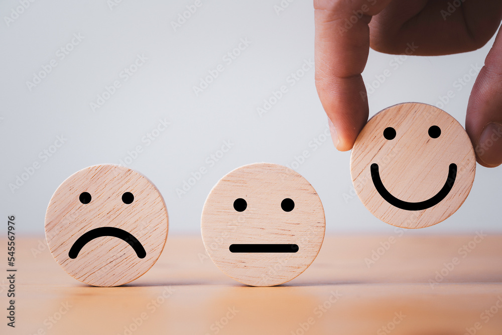Poster Hand holding smile face which print scree on round wooden among regular and sad emotion for excellent client evaluation after customer use product and service concept.