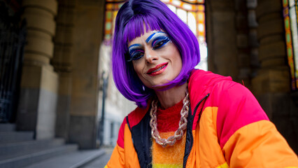 Drag queen in her colorful clothes strolls through the city listening to music and drinking coffee