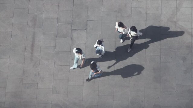 Verical aerial view of People walk cast dark shadows from sun onto concrete gray surface.