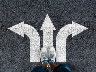 man legs in sneakers standing on road with three direction arrow choices, left, right or move...