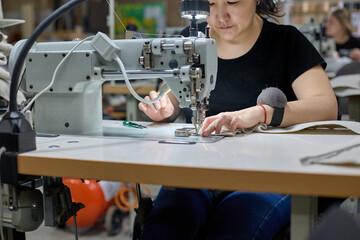 Seamstress or an employee of an Asian textile factory sewing on an industrial sewing machine. The...