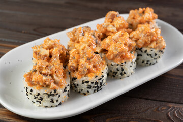 Japanese sushi volcano roll with eel on top and sesame inside, side view . Served on on white plate. Dark wooden background