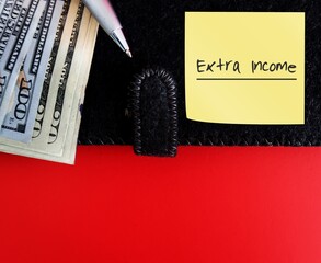 Pen, dollars cash money, black notebook with note written EXTRA INCOME on red copy space...