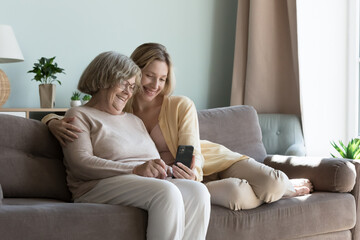Young adult granddaughter and older grandmother using smart phone at home. Multi generational women...