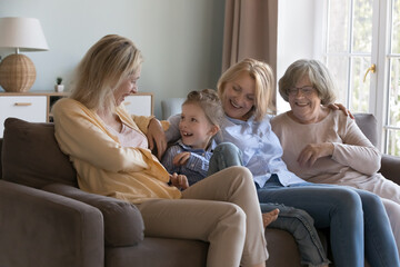 Little girl spend time with loving mom, grandmother and elderly great-grandmother sit together on sofa laughing play feel happy. Multi-generational women enjoy communication, having friendly relations