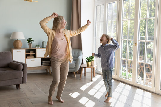 Young woman with little daughter dancing barefoot on warm wooden floor with underfloor heat system at cozy modern house, move to music look carefree and happy. Hobby, active pastime of family at home