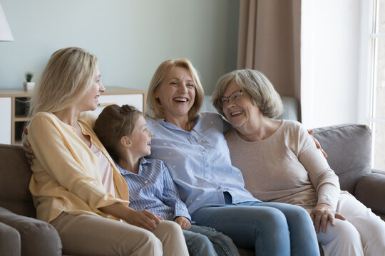Cheerful multi generational attractive younger and older women resting seated on sofa at home, laughing enjoy friendly, warm communication, spend leisure time together feel happy. Family ties, love