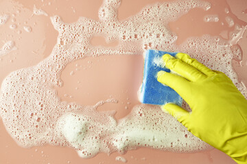 Fototapeta premium a hand in a shopping glove wipes soap suds from a pink background with a sponge