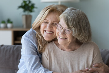 Overjoyed loving middle-aged daughter cuddles her smiling grey-haired elderly retired mom feeling love, enjoy time together, showing care, close up. Daughterhood, Mothers Day congrats, family bonding