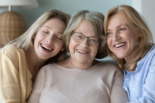 Three different age and generation women portrait. Happy elderly grandma, mature daughter, millennial loving granddaughter sit on sofa laughing enjoy time together and harmonic relation, close up shot