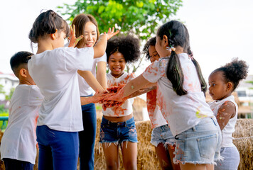 Group of different ethnic little child join their hands together to express support and collaborate also their clothes stain with multicolor after they play with color painting.
