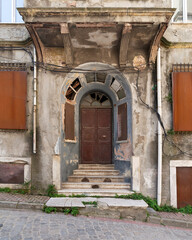 Fototapeta na wymiar Exterior shot of grungy abandoned entrance with rusted metal door, and stairs, on a cobblestone narrow street 