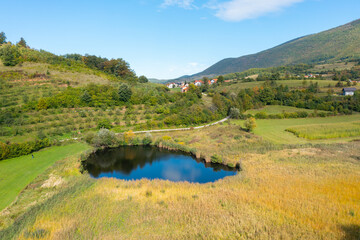 Lake surrounded by meadows, forest and orchard with houses in the distance