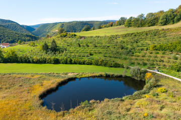 Lake surrounded by meadows, forest and orchard with houses in the distance