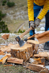 A man in a feathered winter jacket is chopping wood on the mountain with an ax