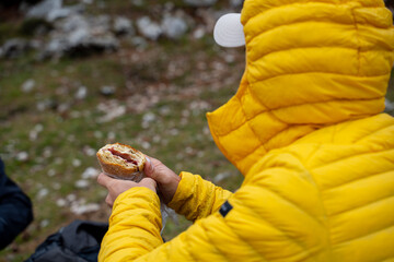 A mountaineer in a winter jacket eats a sandwich on the mountain