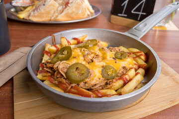 meat in a frying pan with potatoes, hot pepper and cheese on a wooden table. lunch at the cafe.