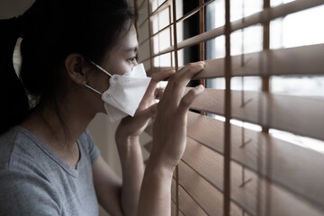 Sick woman of corona virus looking through the window and wearing mask protection and recovery from the illness in home as self quarantine to prevent infection