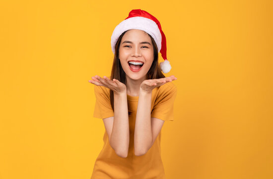 Cheerful beautiful Asian woman wearing red Christmas hat and in orange t-shirt and stand on orange background.