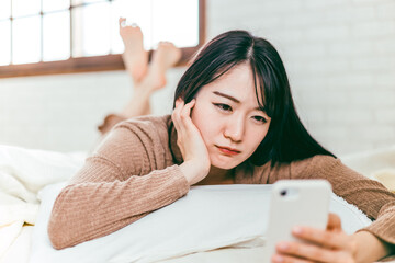 ベッドルームでスマホを見ながら迷惑電話に怒るパジャマ姿の日本人女性
