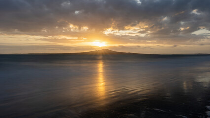 Fototapeta na wymiar Sunrise over the top of Rangitoto Island. Milford Beach, Auckland.