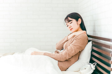 ベッドルームで肩こり・寝違えに悩む日本人女性

