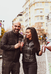Romantic couple  in casual outfits toasting with champagne  outdoors and  posing on streets of european city. Beautiful woman clinking with her husband.Happy couple with a glass of wine  celebrating 