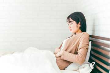 ベッドルームで腹痛・生理痛に悩む日本人女性
